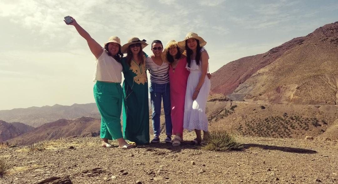 Five women in sun hats pose together on a ridge in the Atlas Mountains